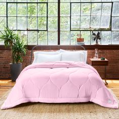 a bed with pink comforter and pillows in front of a window next to a potted plant