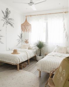 two beds in a room with white walls and palm trees on the wall behind them