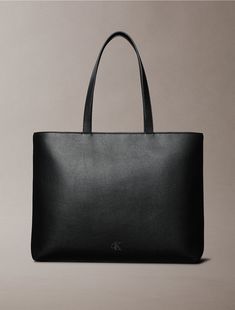 A modern classic, this tote bag features ample storage space for all the essentials. Crafted from durable faux leather with a fine pebbled texture. Finished with a tonal embossed monogram logo for iconic styling.  Material: 100% Polyurethane. Modern Black Tote Bag, Black Structured Shopping Bag, Structured Black Shopping Bag, Black Tote Bag In Signature Coated Canvas, Luxury Tote Bag With Gunmetal Hardware, Women Accessories Bags, Monogram Logo, Modern Classic, Calvin Klein