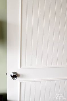 a white door with a black handle on the front and side paneled wall behind it