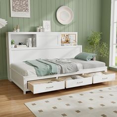 a white bed with drawers underneath it in a green room next to a large window