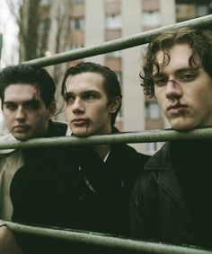 three young men standing next to each other in front of a metal fence and building