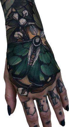 a woman's hand with green and black tattoos on her left arm, holding a butterfly