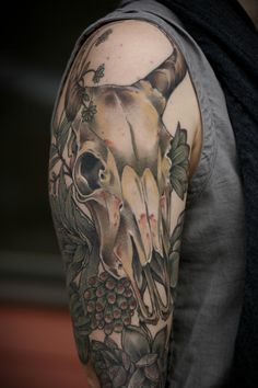 a man with a tattoo on his arm has a cow skull and flowers in it