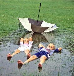 two small children laying in the rain with an umbrella over them and one child lying on it's back