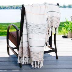 a white and black blanket sitting on top of a wooden chair next to a lake