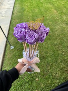 purple roses in a clear glass vase with butterflies on top, held by someone's hand