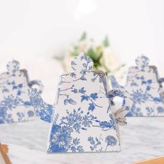 three blue and white ceramic teapots on a table with flowers in the background