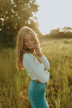 a woman standing in a field with her hands on her head and looking at the camera