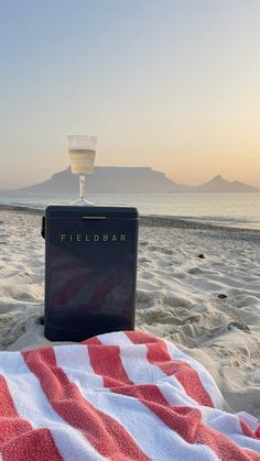 a cooler sitting on top of a beach covered in a blanket next to the ocean