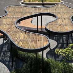 a wooden bench sitting on the side of a road next to a parking lot filled with lots of green plants