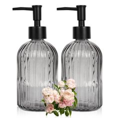 two clear glass soap dispensers with flowers in front of them on a white background