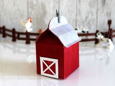 a small red barn with a white roof and two chickens on the fence behind it