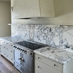 a kitchen with marble counter tops and stainless steel oven hood over the stove, along with white cabinets