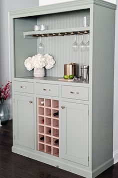 a gray cabinet with wine glasses and vases on the top, filled with white flowers