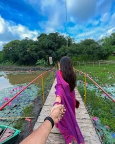 a person holding the hand of another person on a bridge over a river with lily pads