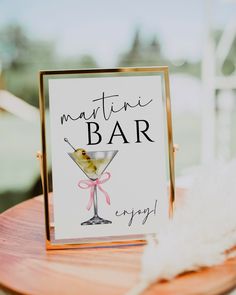 a martini bar sign sitting on top of a wooden table next to a white feather