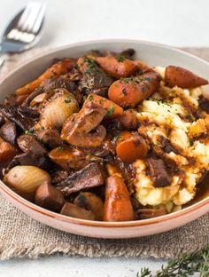 a bowl filled with meat and potatoes on top of a table next to a fork