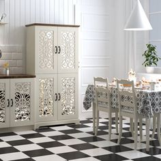 a kitchen with black and white checkered flooring, cabinets and a dining table