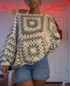 a woman standing in front of a christmas light wearing shorts and a crocheted sweater