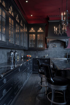 an elegant kitchen with black cabinets and dark wood flooring is lit by chandeliers