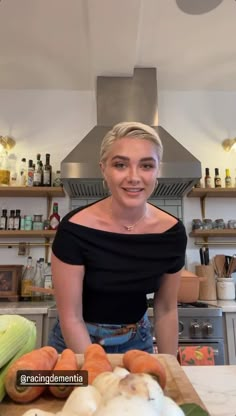 a woman standing in front of a cutting board with carrots and onions on it