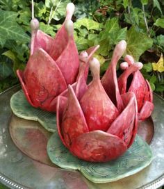 three red flowers sitting on top of a metal platter in the middle of some plants