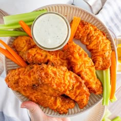 a person holding a plate with chicken wings and carrots next to a bowl of ranch dressing