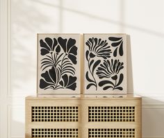 two black and white art pieces sitting on top of a wooden cabinet next to each other