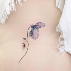 a small flower tattoo on the side of a woman's stomach, it is purple and blue