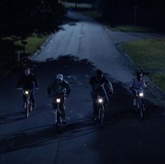 three people riding their bikes at night in the dark with headlights on and one person wearing a helmet