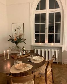 a wooden table with plates and glasses on it in front of a large arched window