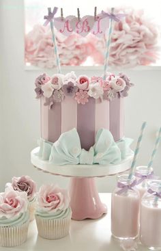 a pink and purple cake sitting on top of a table next to cupcakes