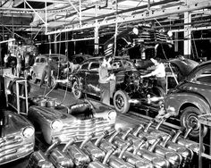 an assembly line with cars being worked on by men in suits and ties, while another man is working on the car