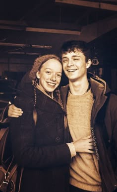 a man and woman standing next to each other in front of a building with their arms around each other