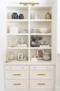 a white bookcase filled with lots of books next to a wall mounted shelf full of vases