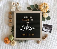 a baby announcement surrounded by pumpkins, leaves and other items on a white blanket