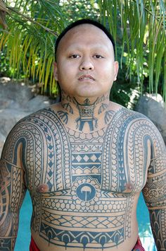 a man with tattoos on his chest standing in front of a pool and palm tree