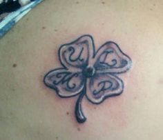 a four leaf clover tattoo on the back of a woman's shoulder