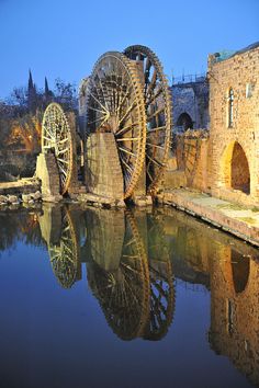 an old water wheel sitting in the middle of a body of water next to a stone building