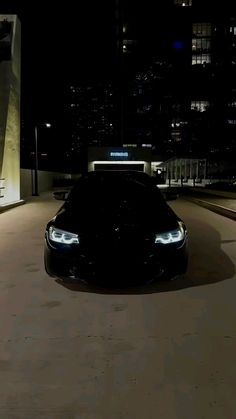 a black sports car parked in front of a tall building at night with lights on