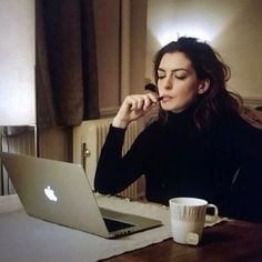 a woman sitting at a table with a laptop and coffee cup in front of her