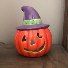 an orange pumpkin with a purple hat on it's head sitting on a table