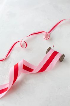 a pink and red ribbon on a white surface with two rolls of tape next to it