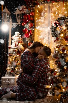 a man and woman kissing in front of a christmas tree with snow falling all around them