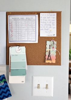 a cork board mounted to the wall with magnets and papers on it next to a light switch