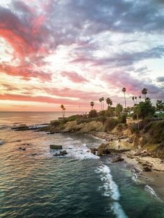 the beach is lined with palm trees as the sun goes down over the water and clouds