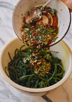 someone is pouring sauce into a bowl filled with green beans and other vegetables on a marble table