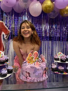 a woman standing in front of a table with cupcakes and cake on it