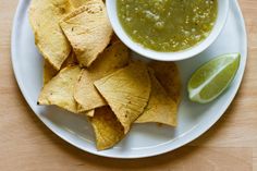 a white plate topped with chips and guacamole next to a slice of lime